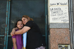 Dos personas se abrazan al lado de una pared con escrituras a favor de Milei el día de su asunción presidencial 2023